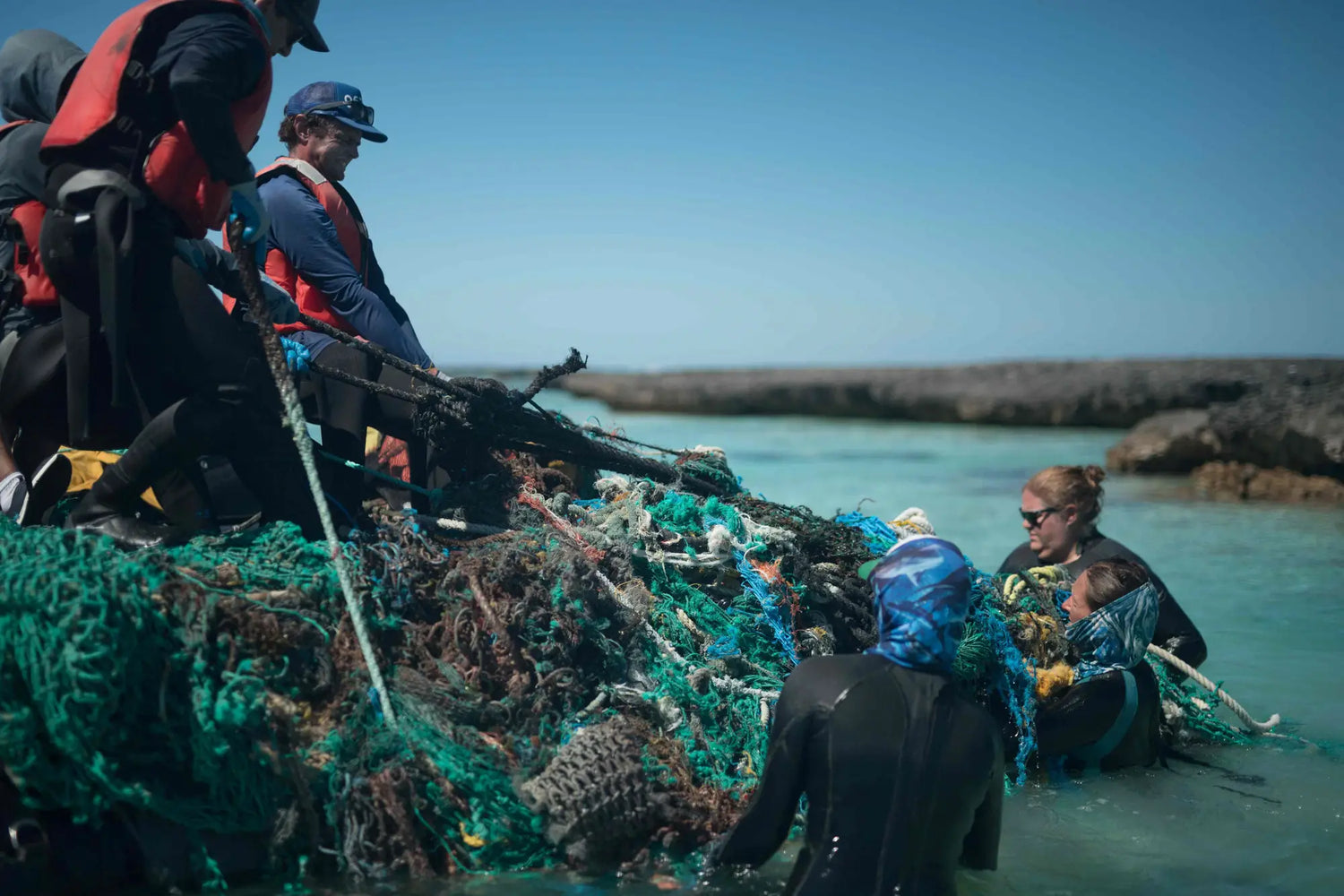 People working to remove large fishing nets in a body of water.