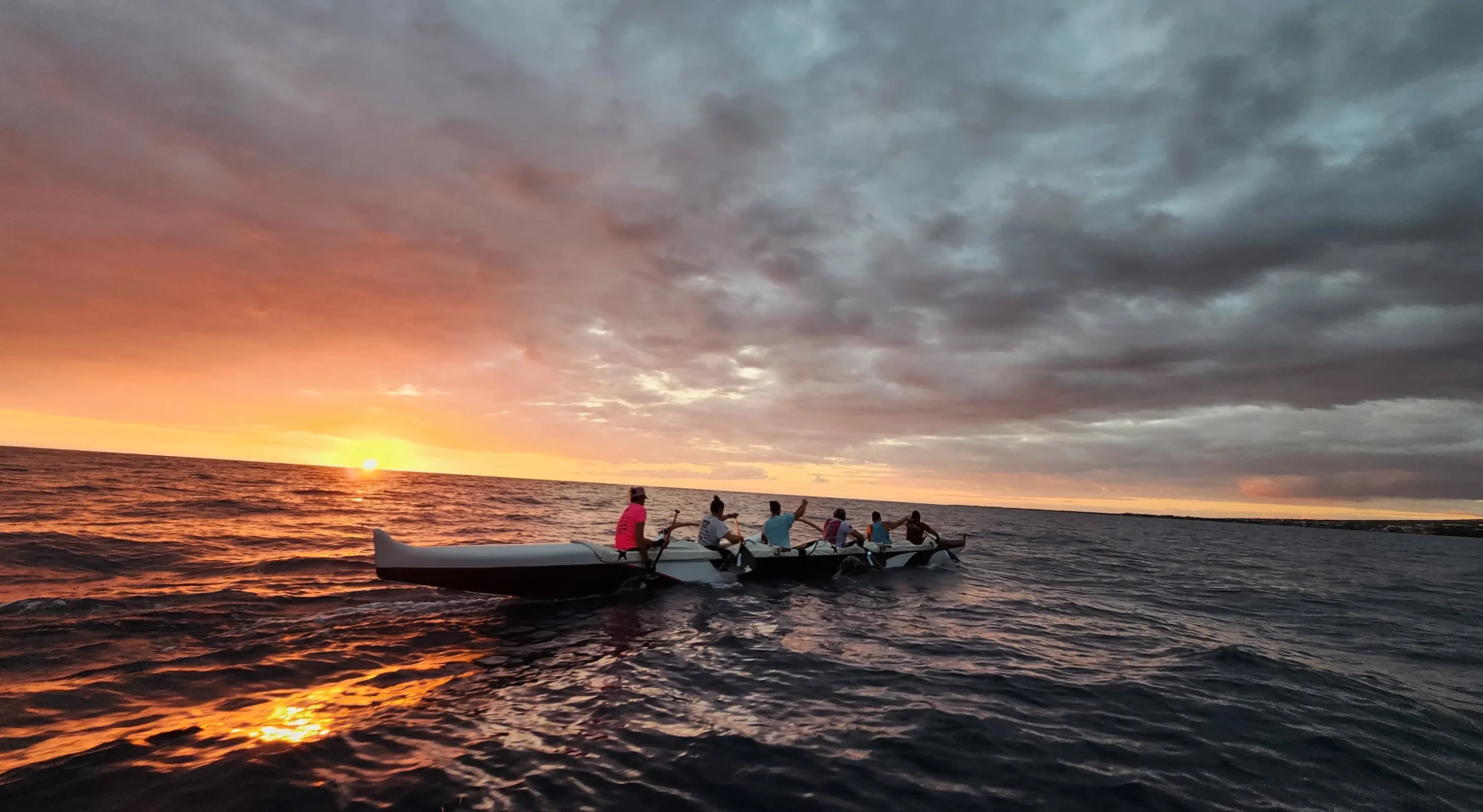 People paddling a canoe on a body of water with a colorful sunset sky.