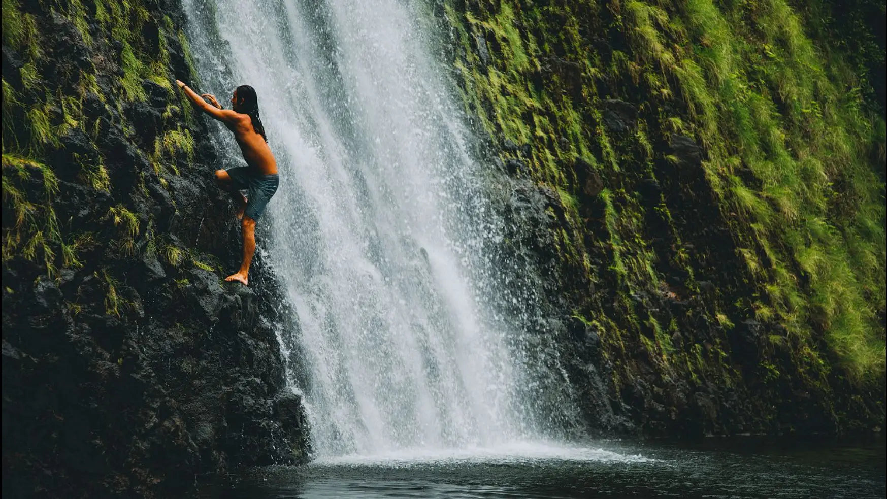 Person climbing a waterfall from a rocky ledge