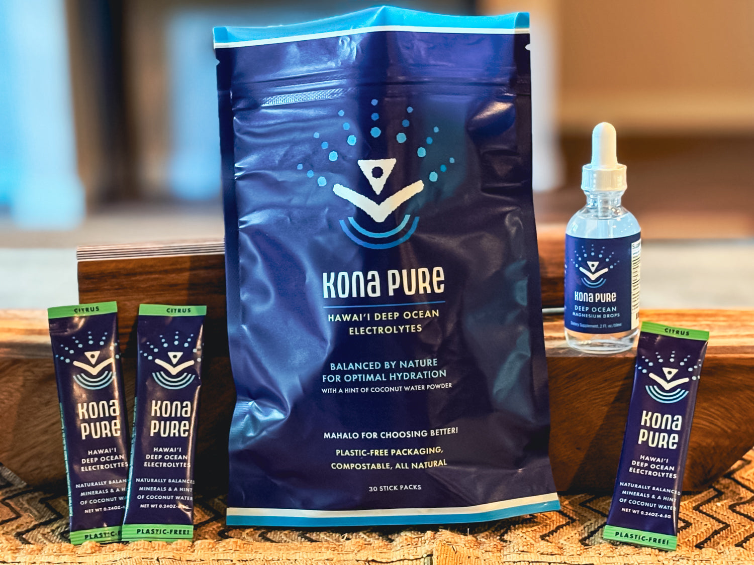 Kona Pure electrolyte powder package with sticks and a bottle on a wooden surface.