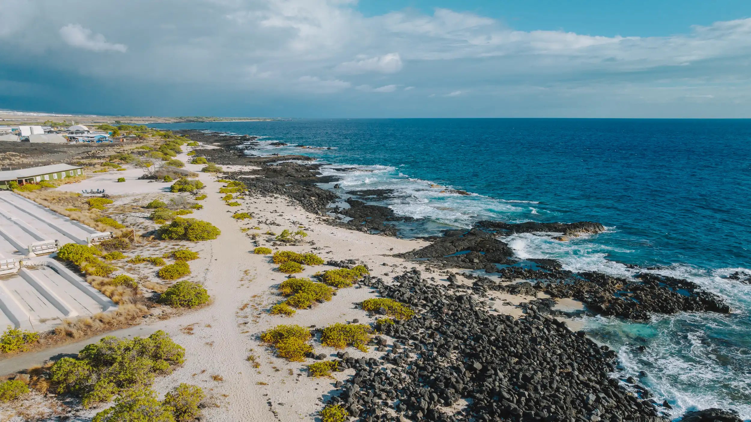 Coastal landscape with rocky shore and ocean waves, under a blue sky with clouds.
