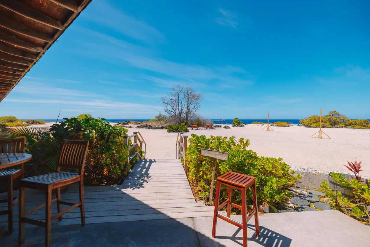 Outdoor seating area with wooden chairs and tables on a deck overlooking a beach and ocean.