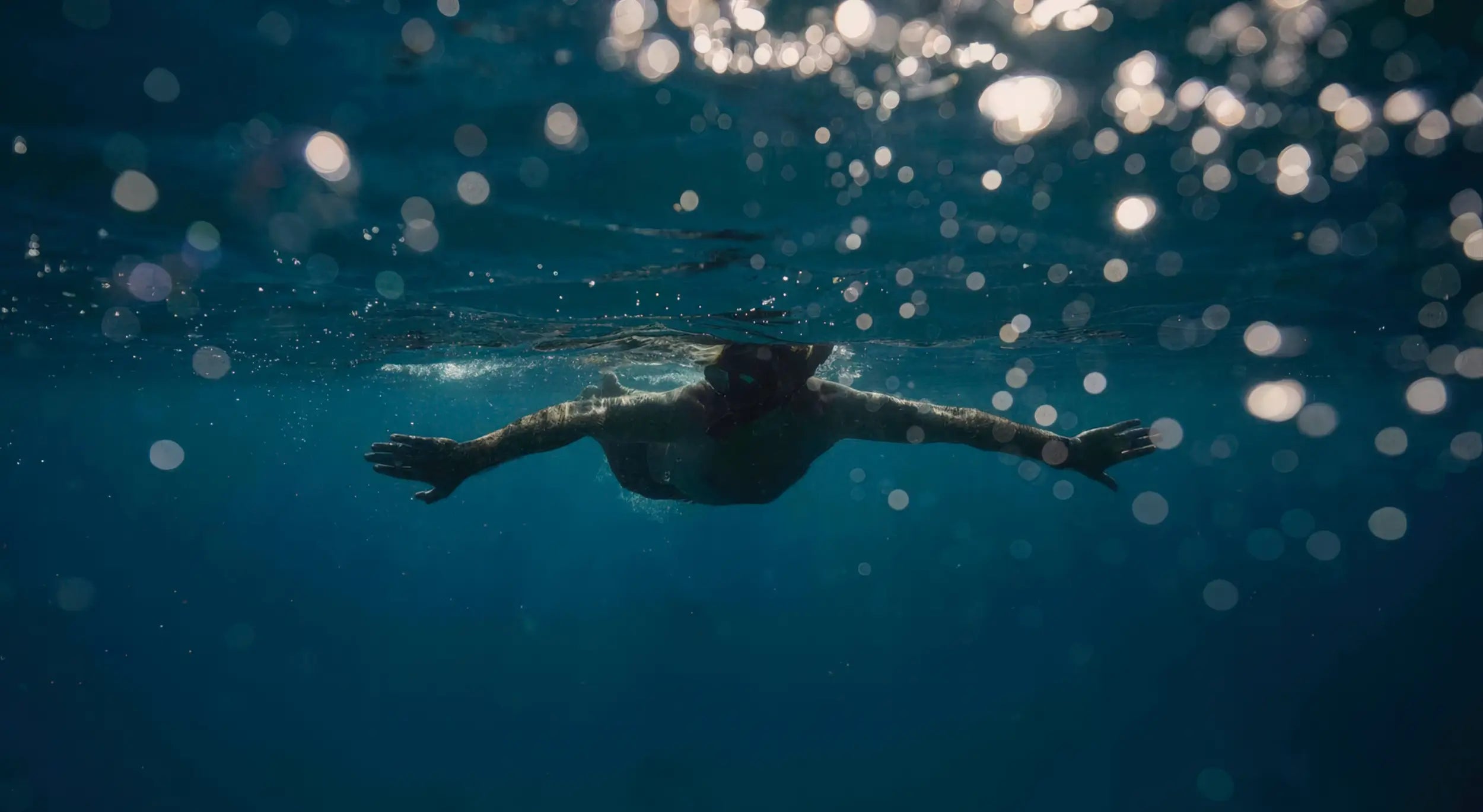 Person swimming underwater with sunlight filtering through the water surface
