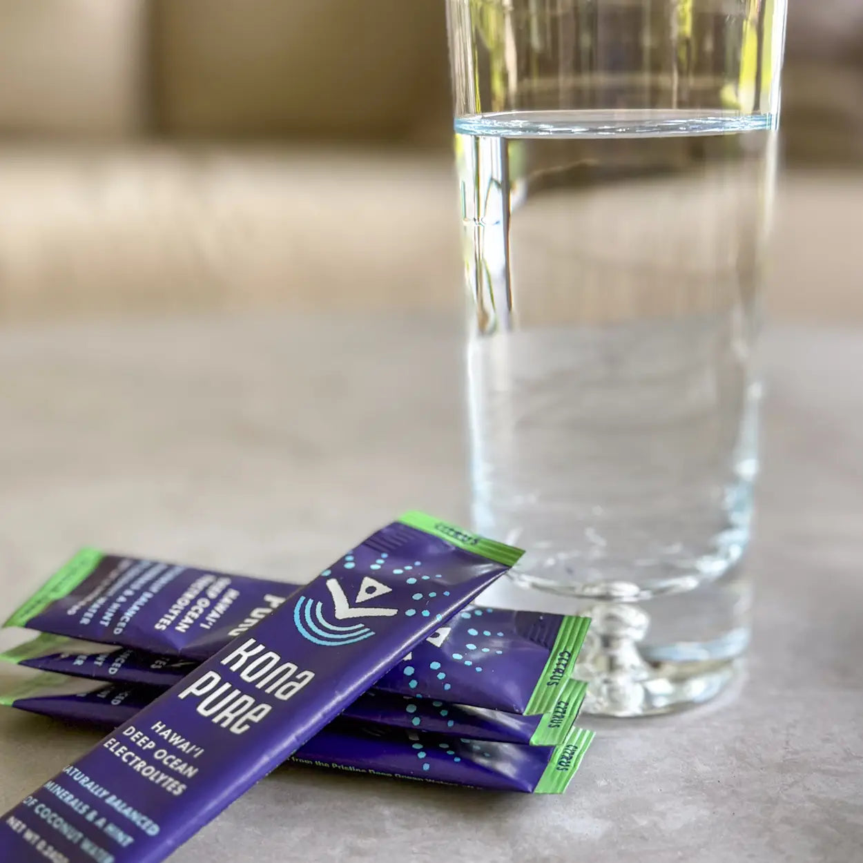 Kona Pure packets with a glass of water on a neutral background